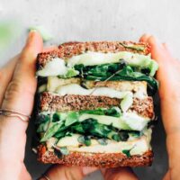 hands holding two green vegan sandwiches with tofu and vegetables