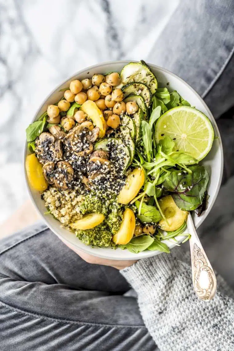 Woman sitting cross-legged and holding vegan buddha bowl with greens, chickpeas and other vegetables