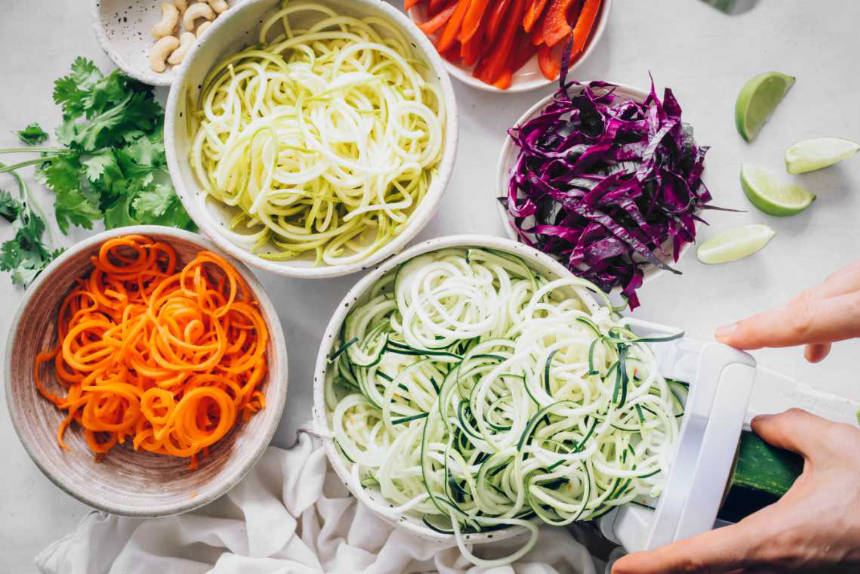 different bowls with spiralized veggies next to a spiralizer on a table
