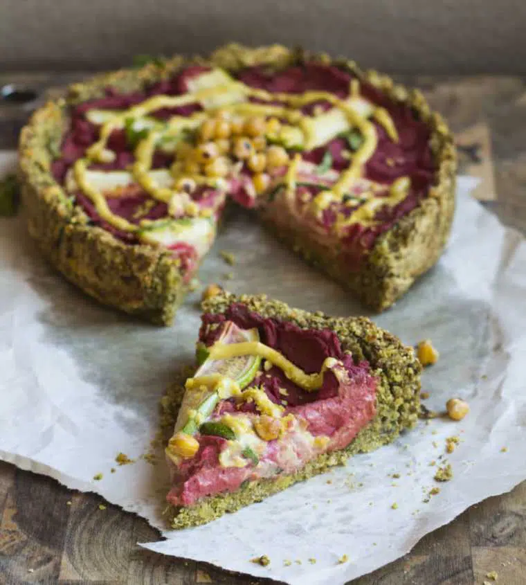 colorful vegan deep pizza with falafel crust and a pink hummus filling on a wooden table