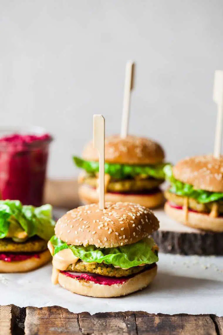 four plant-based burgers with lettuce, vegan patties and beet hummus on a wooden table