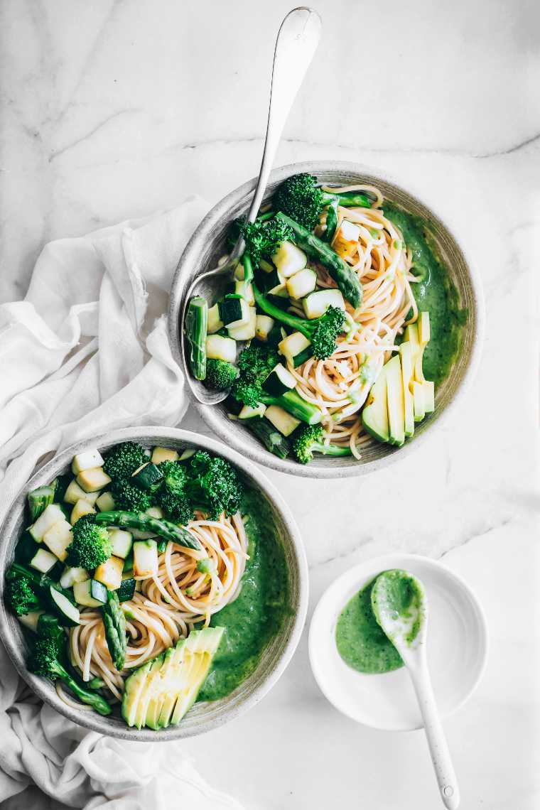 two serving bowls with homemade green hummus pasta and a spoon