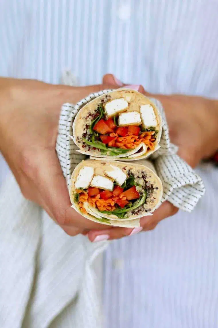 woman in striped shirt and pink nails holds two cut up wraps filled with tofu, veggies and hummus in her hands