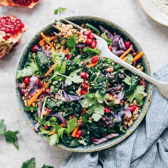 table with pomegranate, towel and a bowl of colorful warm lentil kale salad