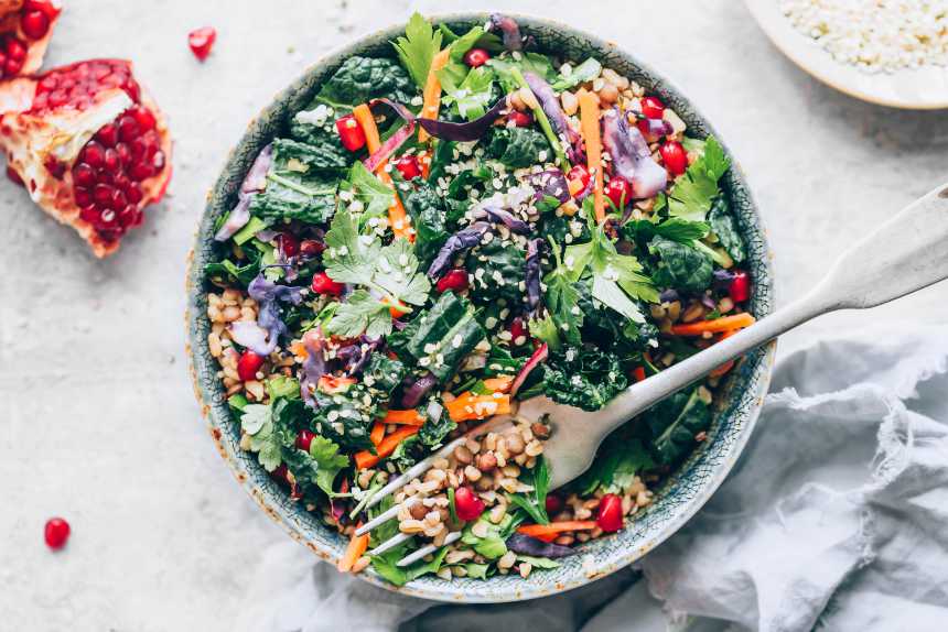 large bowl of warm lentil kale winter salad with pomegranate and a fork