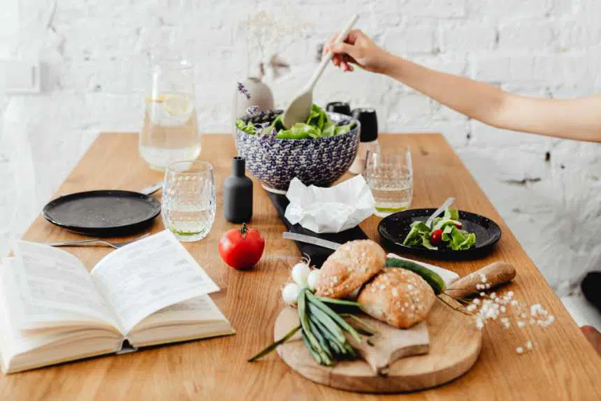 wooden table with a book, glasses, plates, different vegetables and white bread