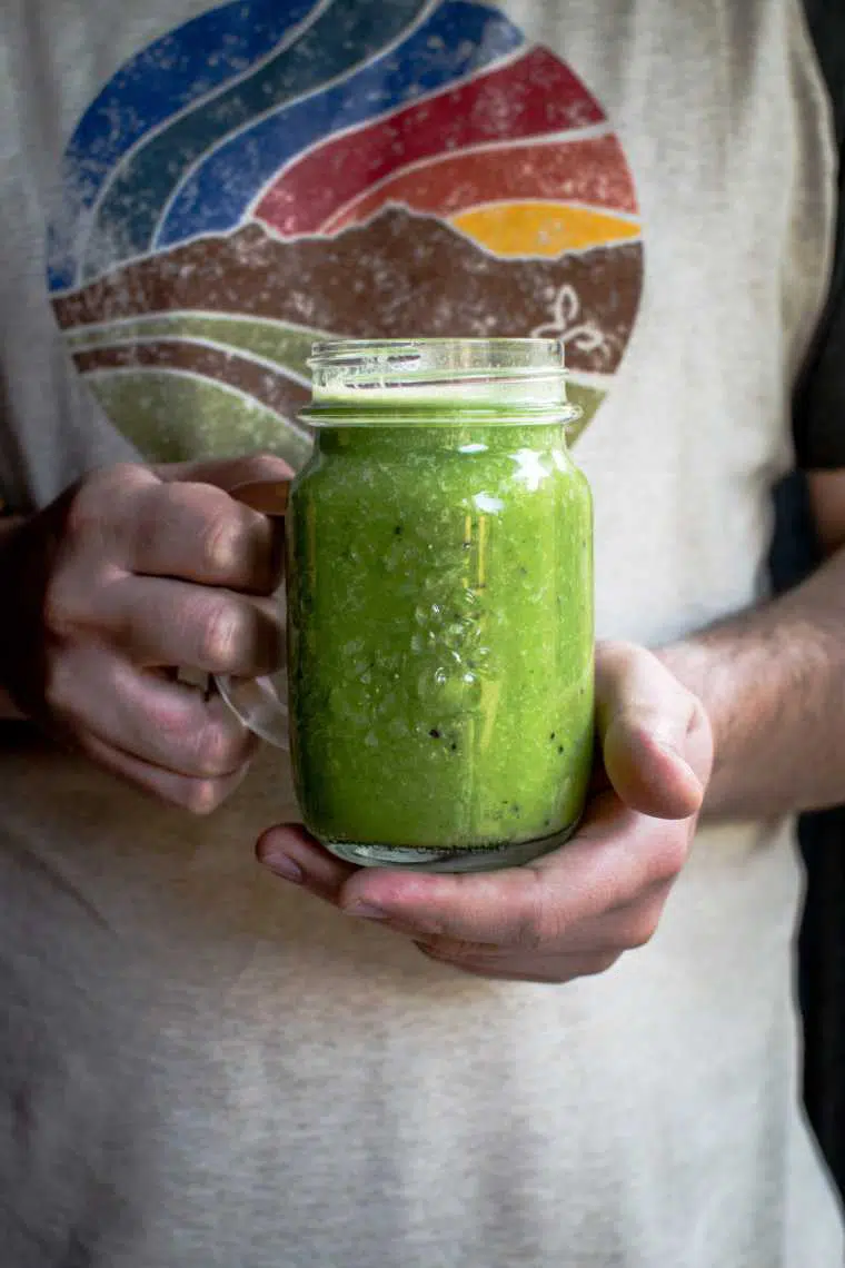 man in colorful shirt holding a glass with homemade green smoothie in his hands
