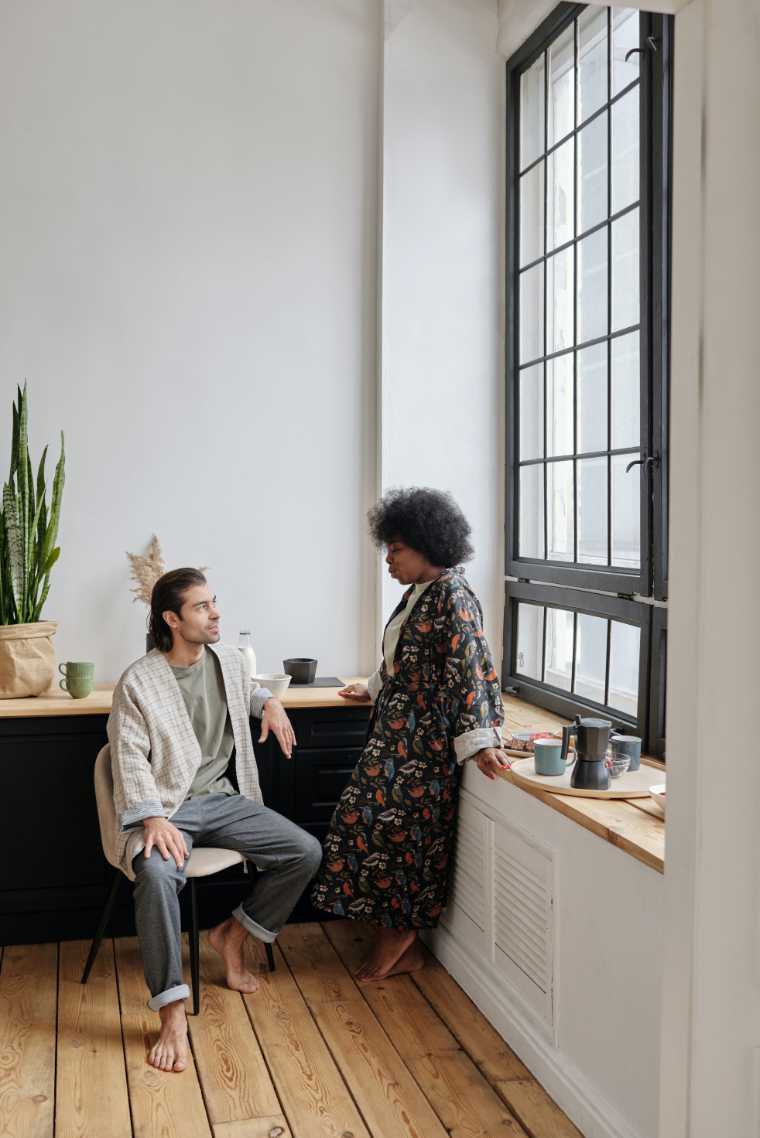 man sitting next to a woman leaning on a window sill and talking friendly