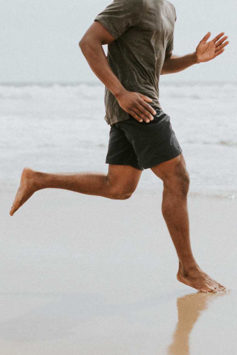black man with short pants and a shirt running at the beach