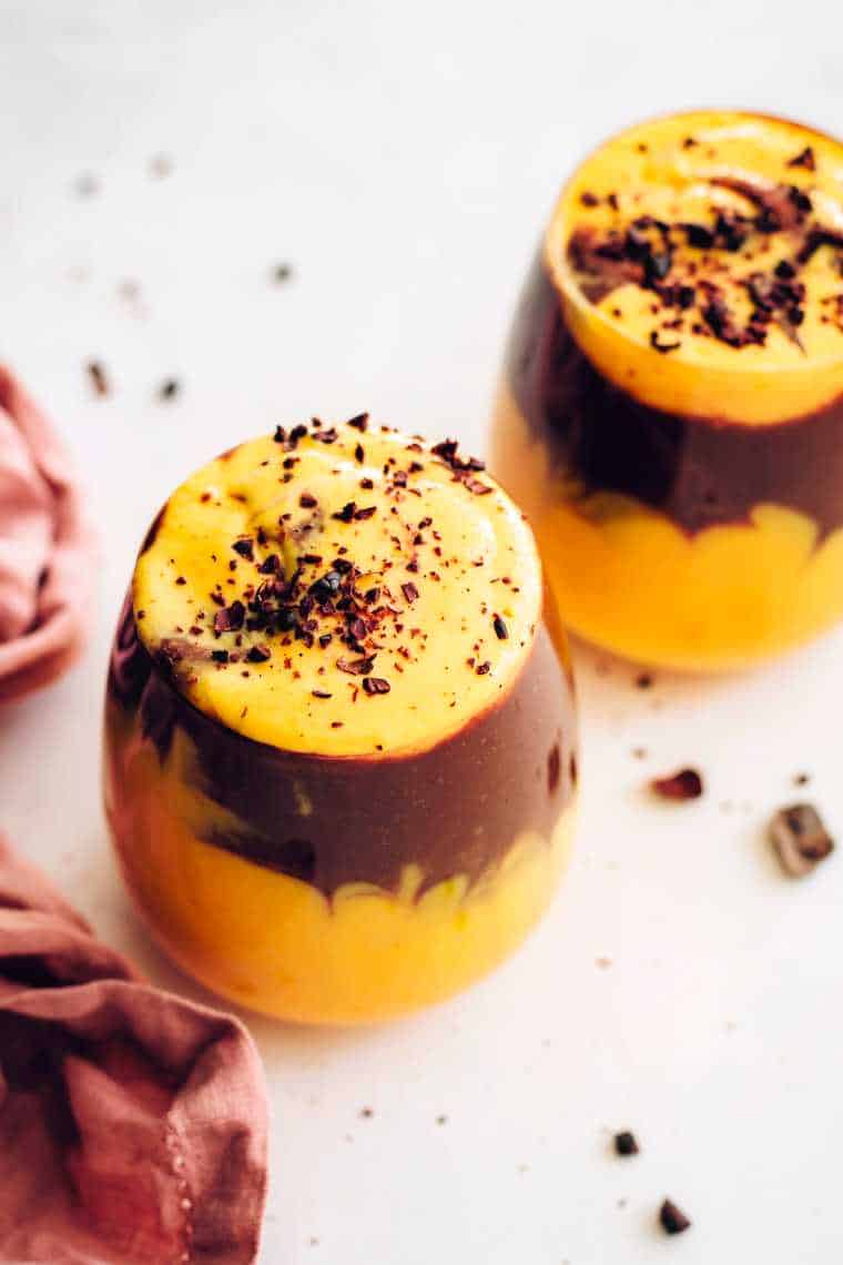 two glasses with layered mango chocolate smoothie and cocoa nibs