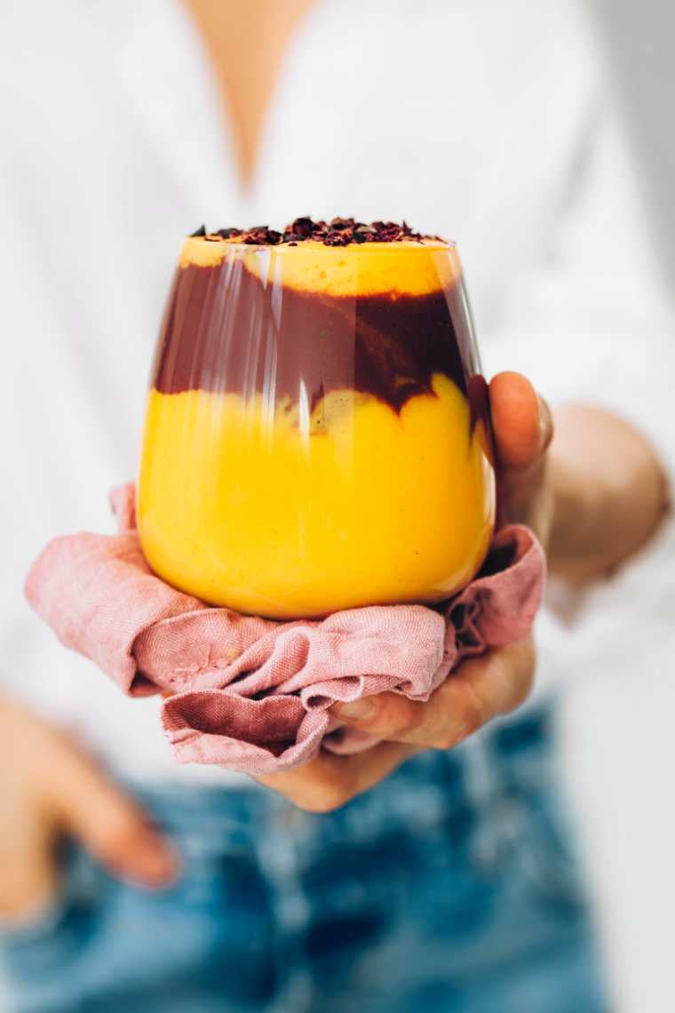 woman in white shirt and jeans holding a glass of mango chocolate smoothie