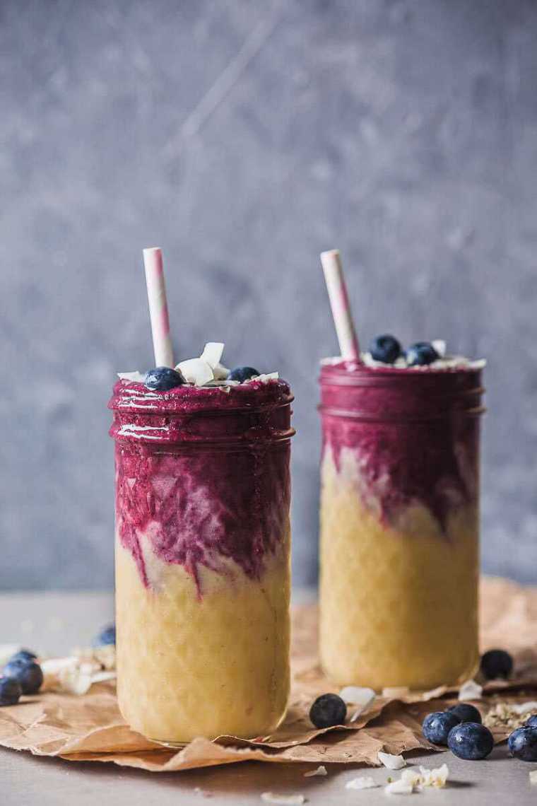 table with two glass jars filled with mango blueberry smoothie and a paper straw each