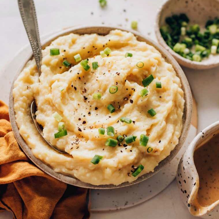 table with a bowl of plant-based mashed potatoes decorated with black pepper and green onion
