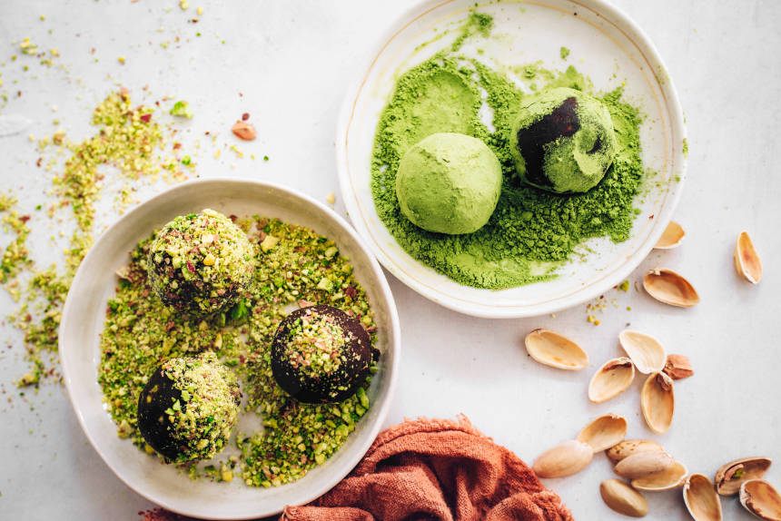 white table with two bowls containing matcha bliss balls and pistachio bliss balls