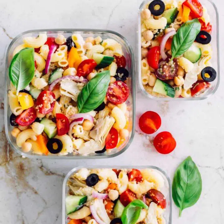 white tables with three glass containers containing colorful vegan quinoa pasta salad with tomatoes, bell pepper and basil