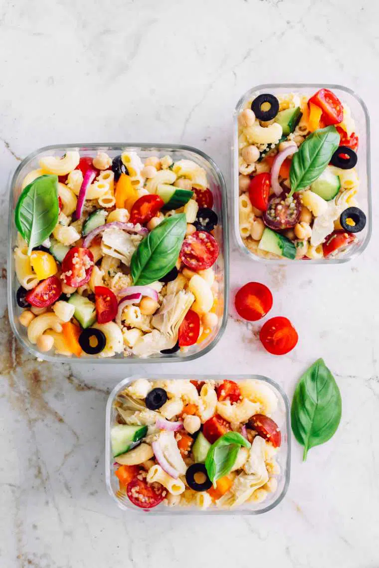 white tables with three glass containers containing colorful vegan quinoa pasta salad with tomatoes, bell pepper and basil