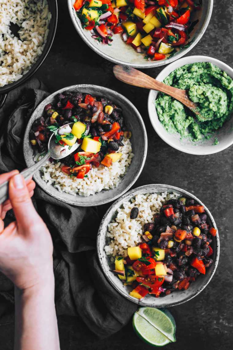 adding mango salsa to bowl with black beans and rice