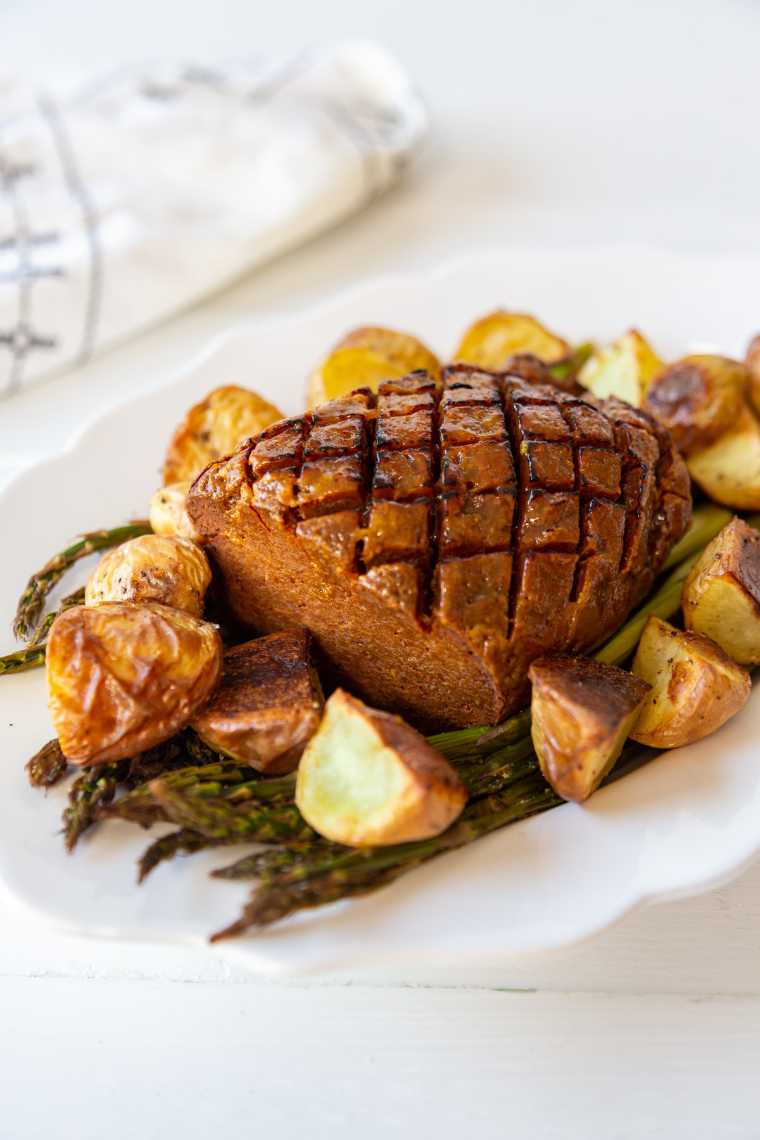 white serving plate with roast potatoes, asparagus and vegan ham