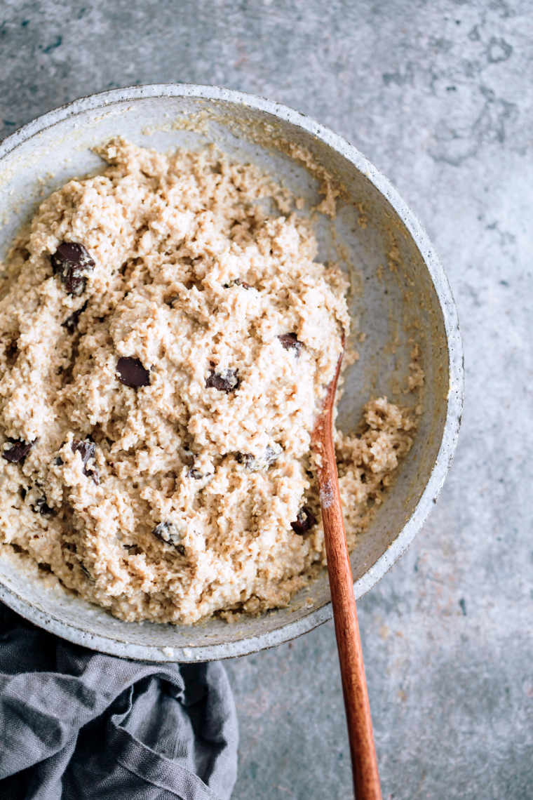 white bowl with a wooden spoon and batter for vegan chocolate chip oatmeal cookies