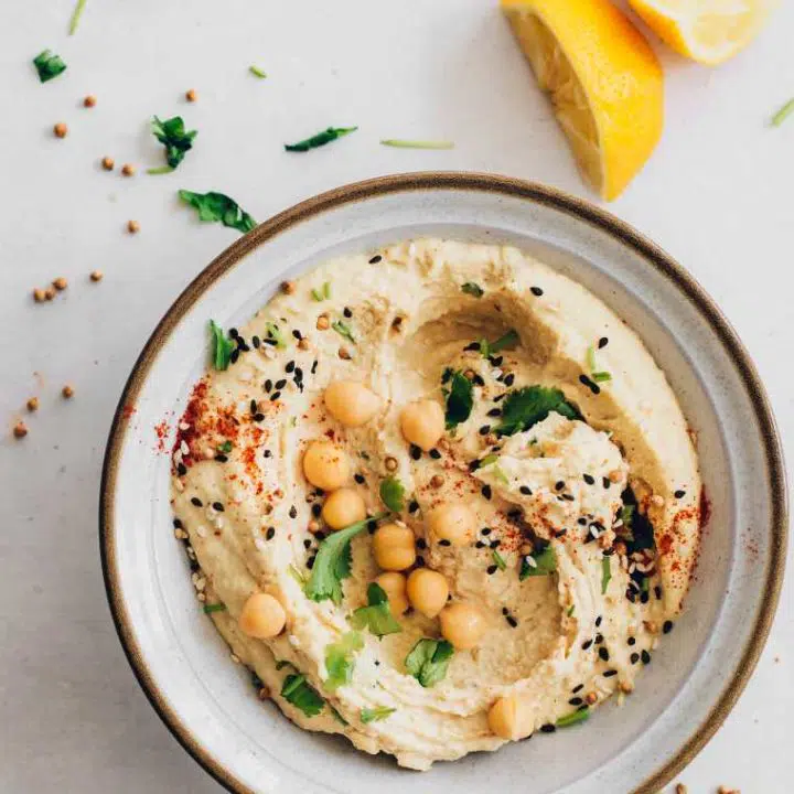 table with a bowl of homemade vegan oil-free hummus topped with spices, black sesame and chickpeas