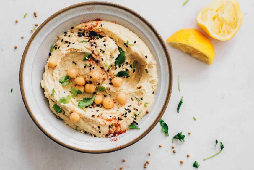 table with a bowl of oil-free vegan hummus decorated with seeds, spices and herbs
