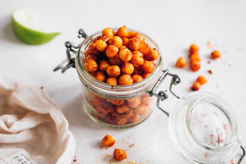 glass jar on a table next to a towel and lime filled which oil-free roasted chickpeas