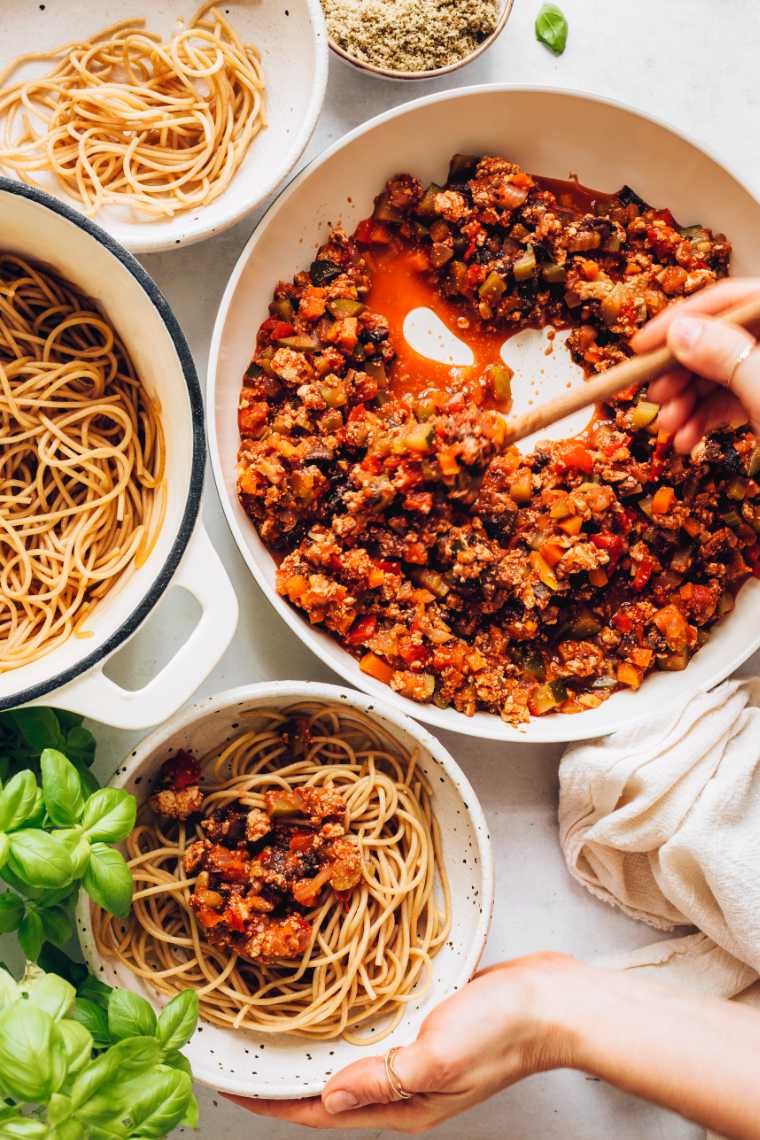table with several bowls of cooked spaghetti that are being topped with vegan bolognese