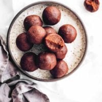 table with a speckled plate on which about a dozen peanut butter bliss balls lie, some of which are half eaten