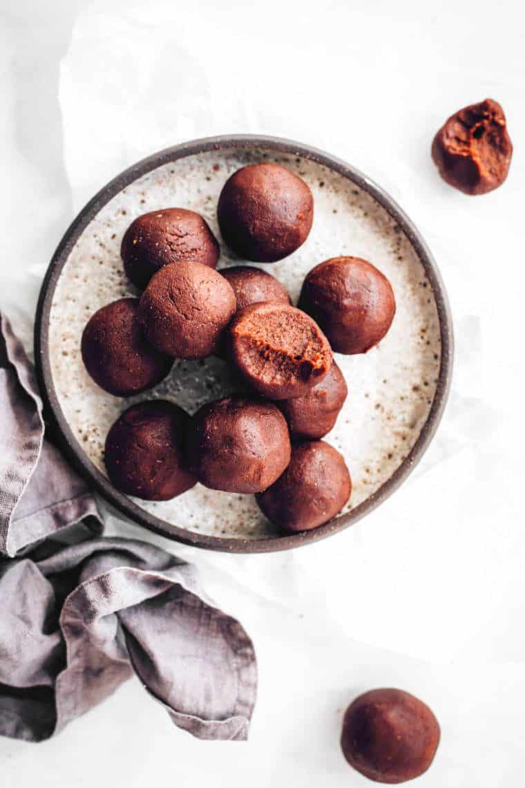 table with a speckled plate on which about a dozen peanut butter bliss balls lie, some of which are half eaten