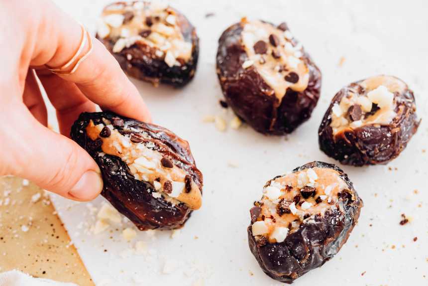 hand holding a peanut butter stuffed date over a plate with more dates