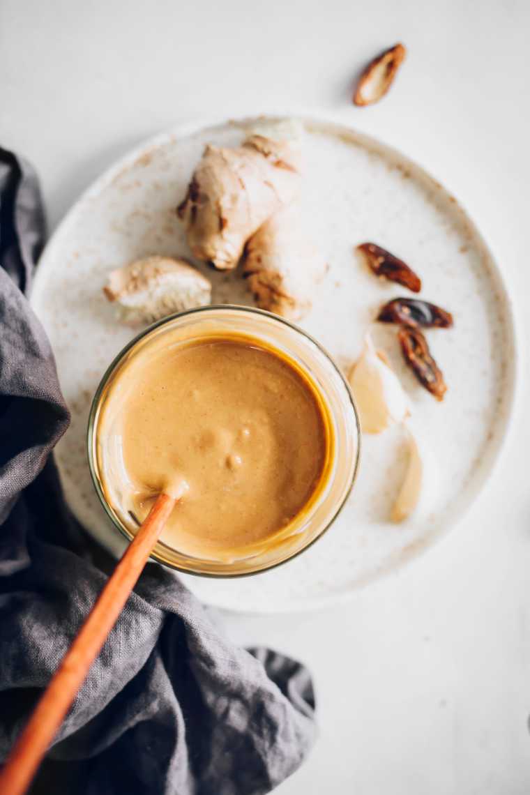 white table with a plate and a glass jar containing vegan peanut butter sauce and a wooden spoon