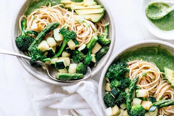 Overhead view of two bowls with spaghetti, green pesto and green vegetables