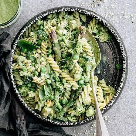 dark bowl of vegan pesto pasta with steamed broccoli and asparagus next to some oil free vegan pesto