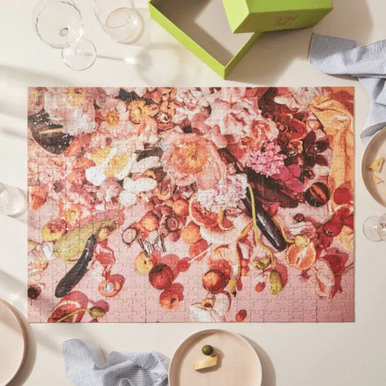 table with a pink art work jigsaw puzzle alongside beverages and snacks