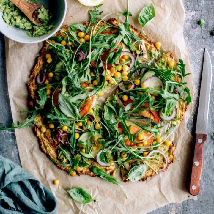 table with parchment paper and freshly baked plant-based cauliflower potato crust pizza with arugula