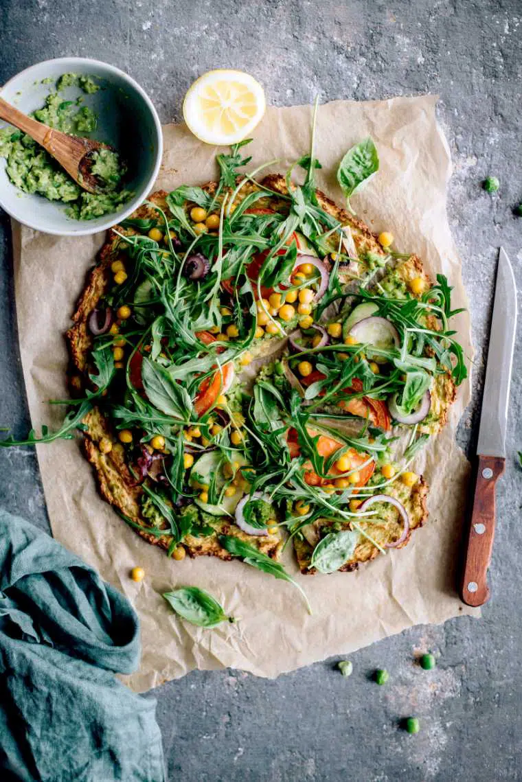 table with parchment paper and freshly baked plant-based cauliflower potato crust pizza with arugula
