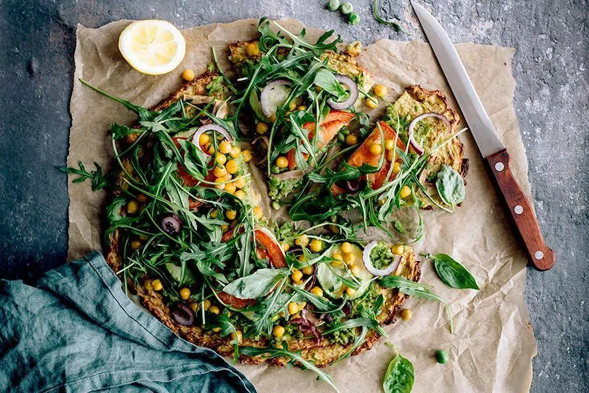 table with parchment paper and freshly baked plant-based cauliflower potato crust pizza next to a knife
