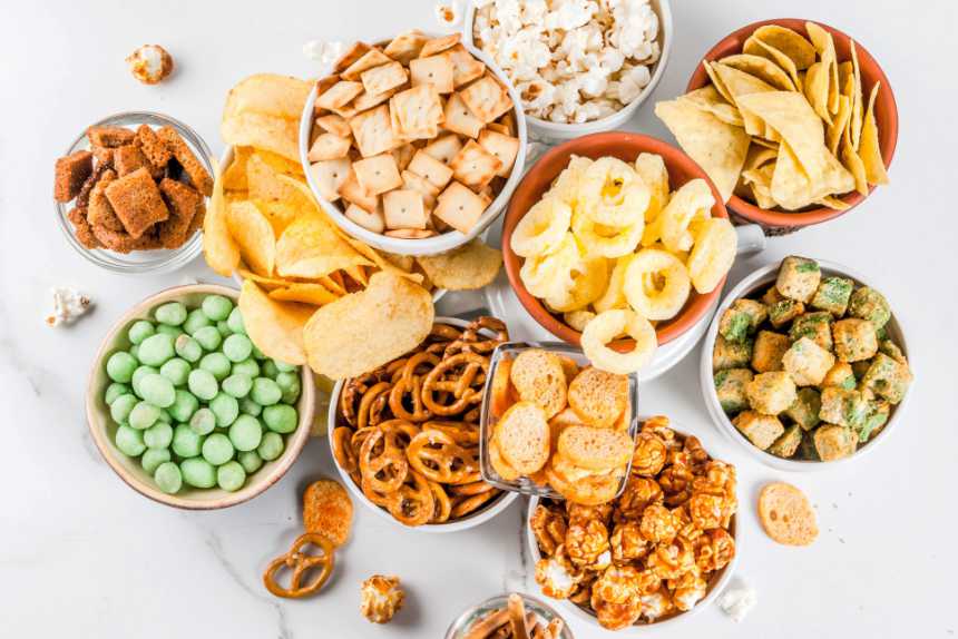 white table with around a dozen of different plant-based snacks you can buy at the store like chips, crackers, pretzels or popcorn