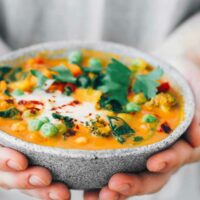 Closeup of woman in grey shirt holding bowl with finished vegan curry in front of her