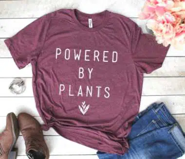 purple colored cotton t shirt with the print "powered by plants" next to a pair of jeans and vegan shoes