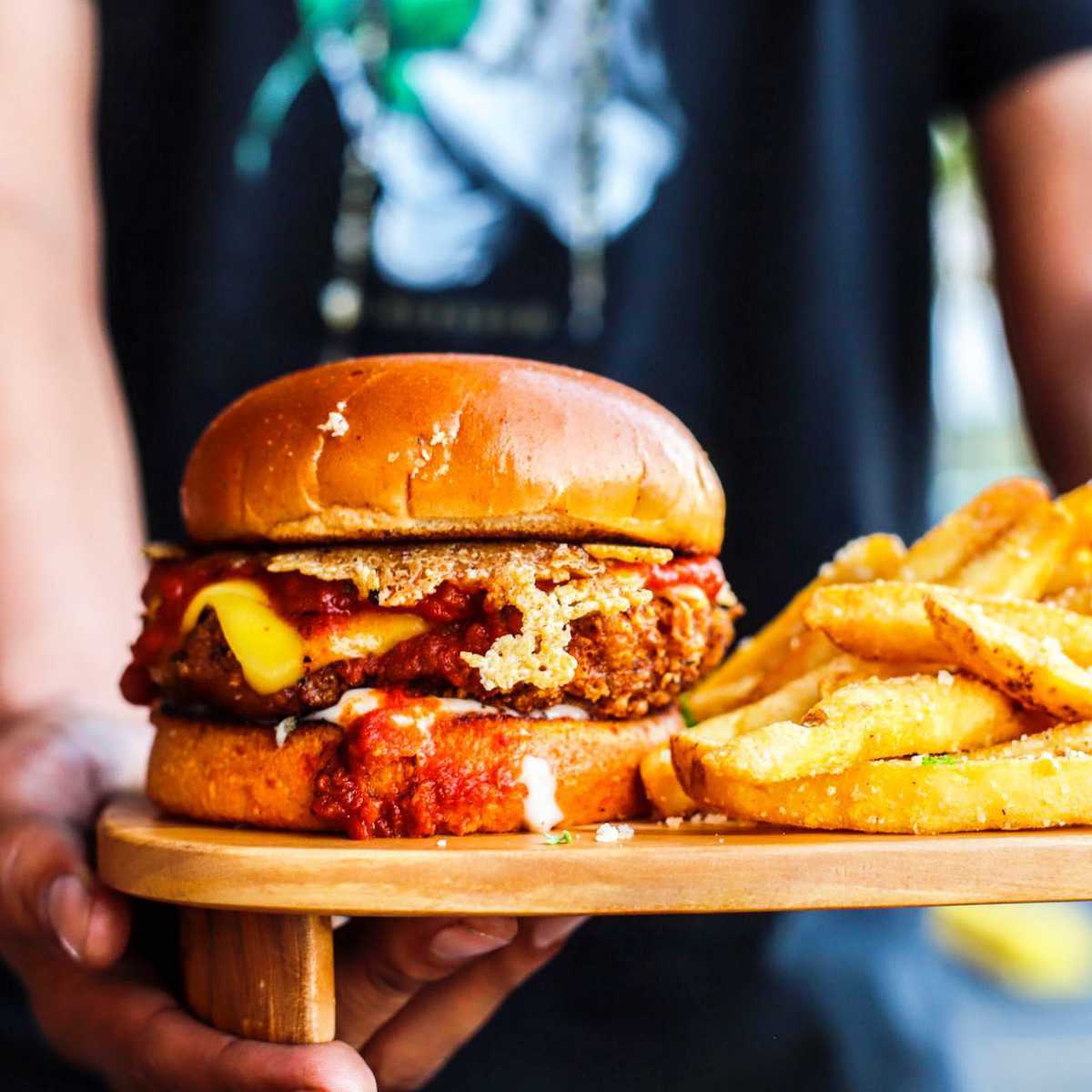 person holding a wooden board with a vegan burger and fries