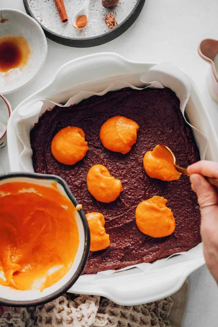 vegan brownie batter in dish being topped with pumpkin puree