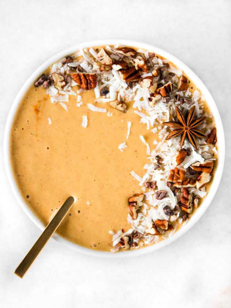 white bowl with a spoon and orange pumpkin chai smoothie topped with winter spices and coconut