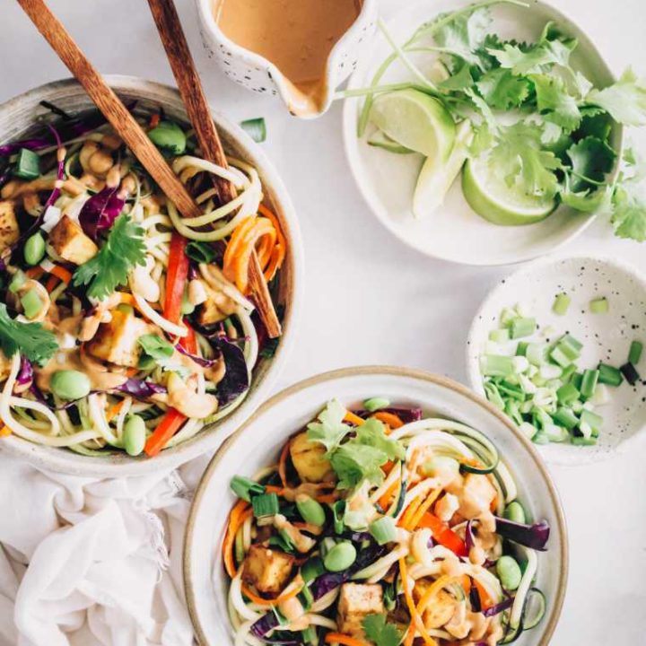 two bowls of colorful spiralized veggies topped with edamame, tofu and a creamy peanut butter sauce