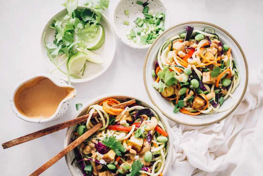 two bowls of colorful raw vegan zoodles with peanut butter sauce and tofu