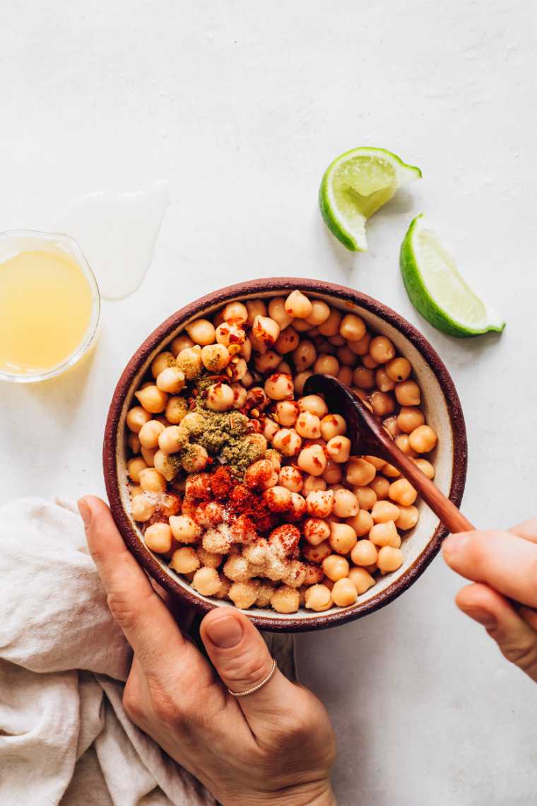 hands holding a bowl with cooked chickpeas and a spoon mixing them with spices
