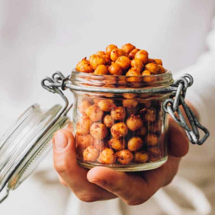 woman in white clothes holing a glass with freshly roasted chili lime chickpeas in her hand
