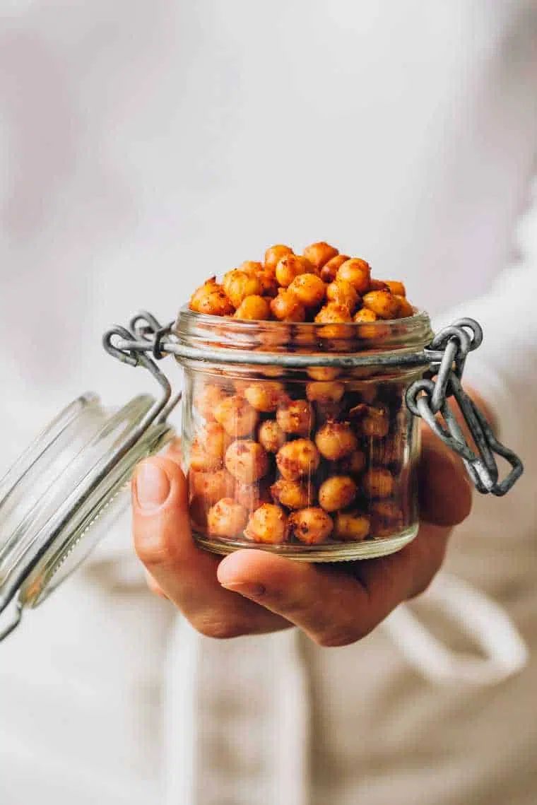woman in white clothes holing a glass with freshly roasted chili lime chickpeas in her hand