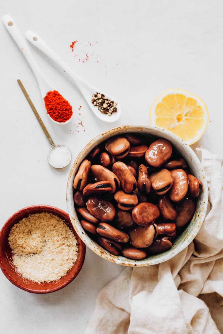 bowl of cooked fava beans next to spices on a table