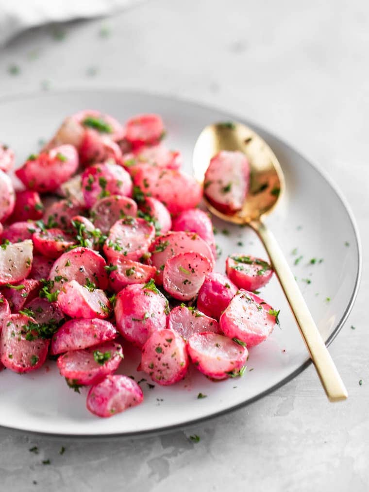 white plate with halved pink roasted radishes and some herbs next to a golden spoon